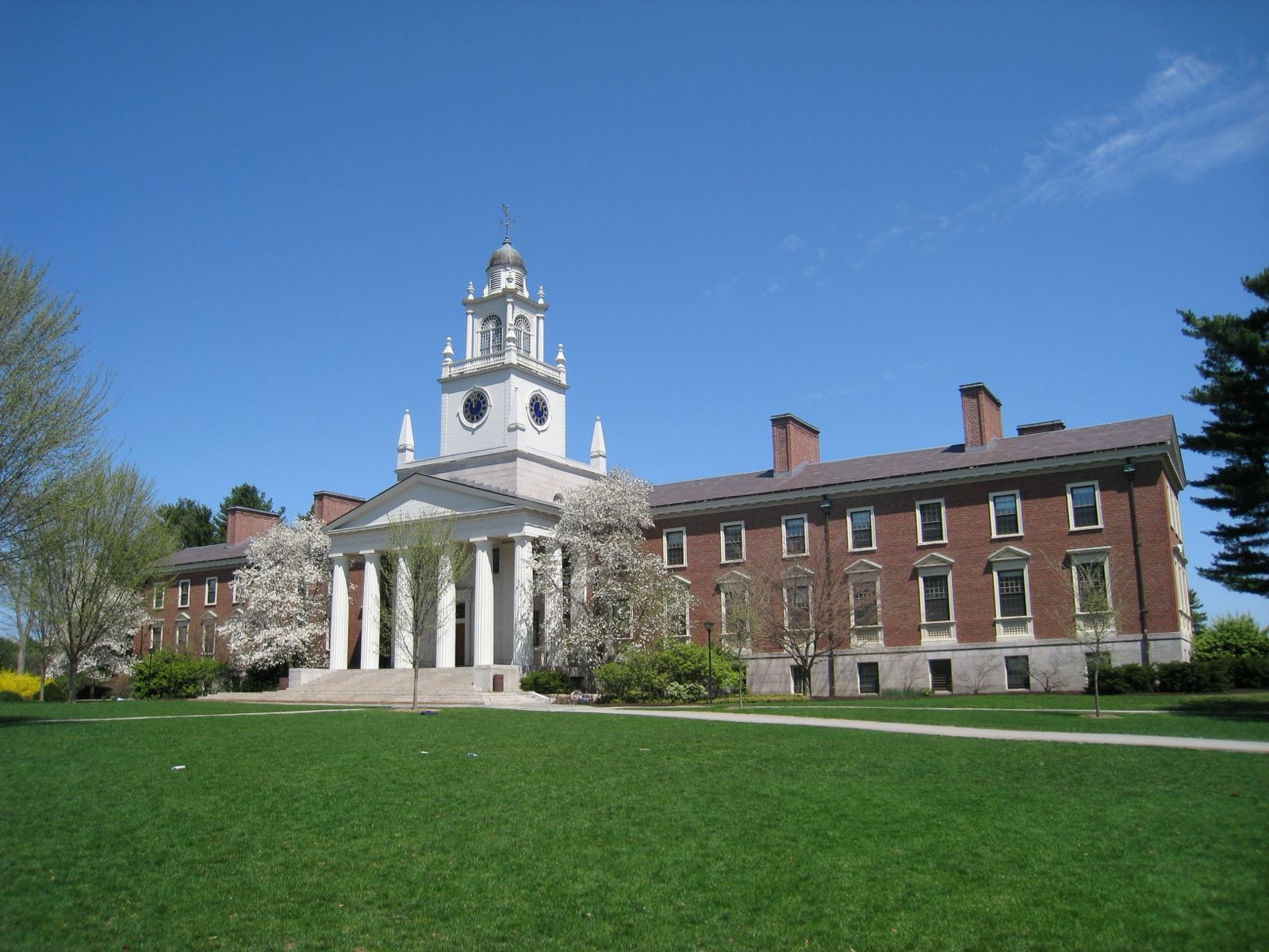 A brick academic hall with a white clock tower across a lawn on the Andover campus